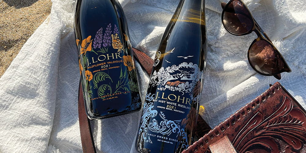 two J. Lohr Monterey Roots wine bottles laying on large cloth on sand
